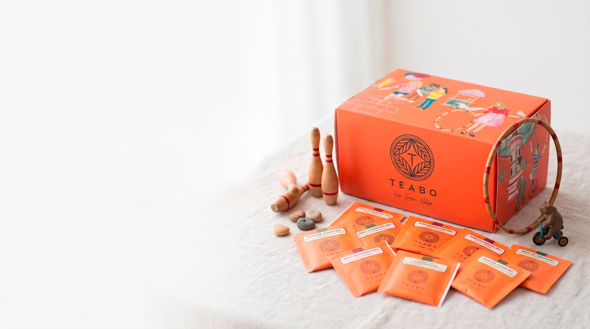 Le coffret Teabo illustré, entouré de sachets de thé et de jouets en bois sur une nappe de lin