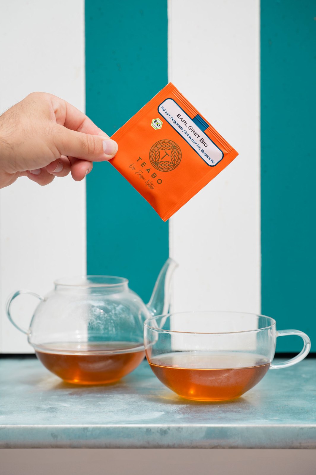 Une main pose un sachet Teabo au-dessus d’une théière